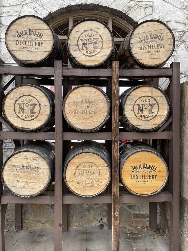 Nine Jack Daniel Distillery and Old No. 7 Brand barrel heads stacked in a wooden rack against a white stone wall in Lynchburg