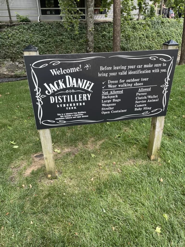 Jack Daniel Distillery welcome sign listing ID requirement, walking shoes, and items not allowed such as backpacks, large bags, weapons, strollers and open containers