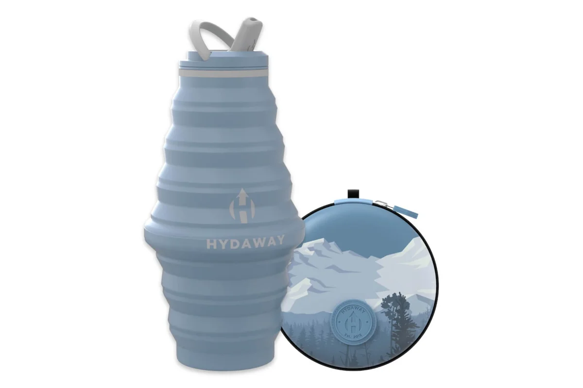 Light blue HYDAWAY 25 oz collapsible bottle expanded next to a round travel case with a mountain print