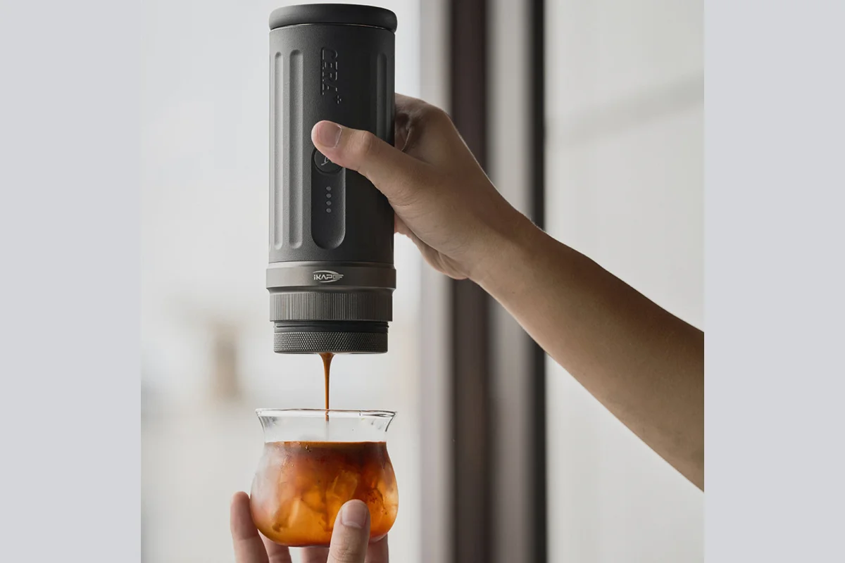 Hand holding the IKAPE Kapo K2 portable espresso maker as it pulls a shot over ice