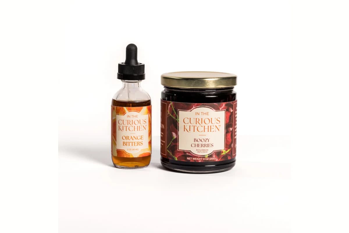 In the Curious Kitchen Orange Bitters dropper bottle beside a jar of Boozy Cherries