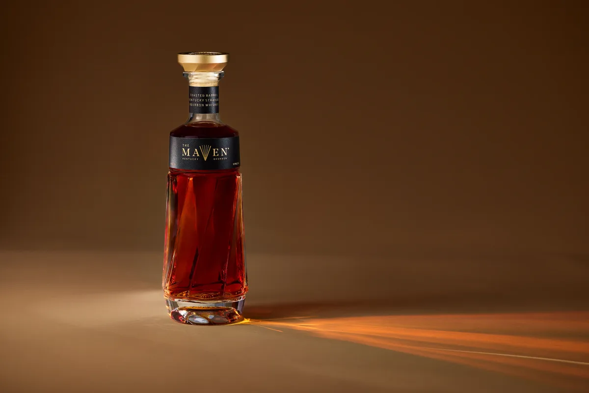 Bottle of The Maven Kentucky Straight Bourbon Whiskey on a warm amber backdrop