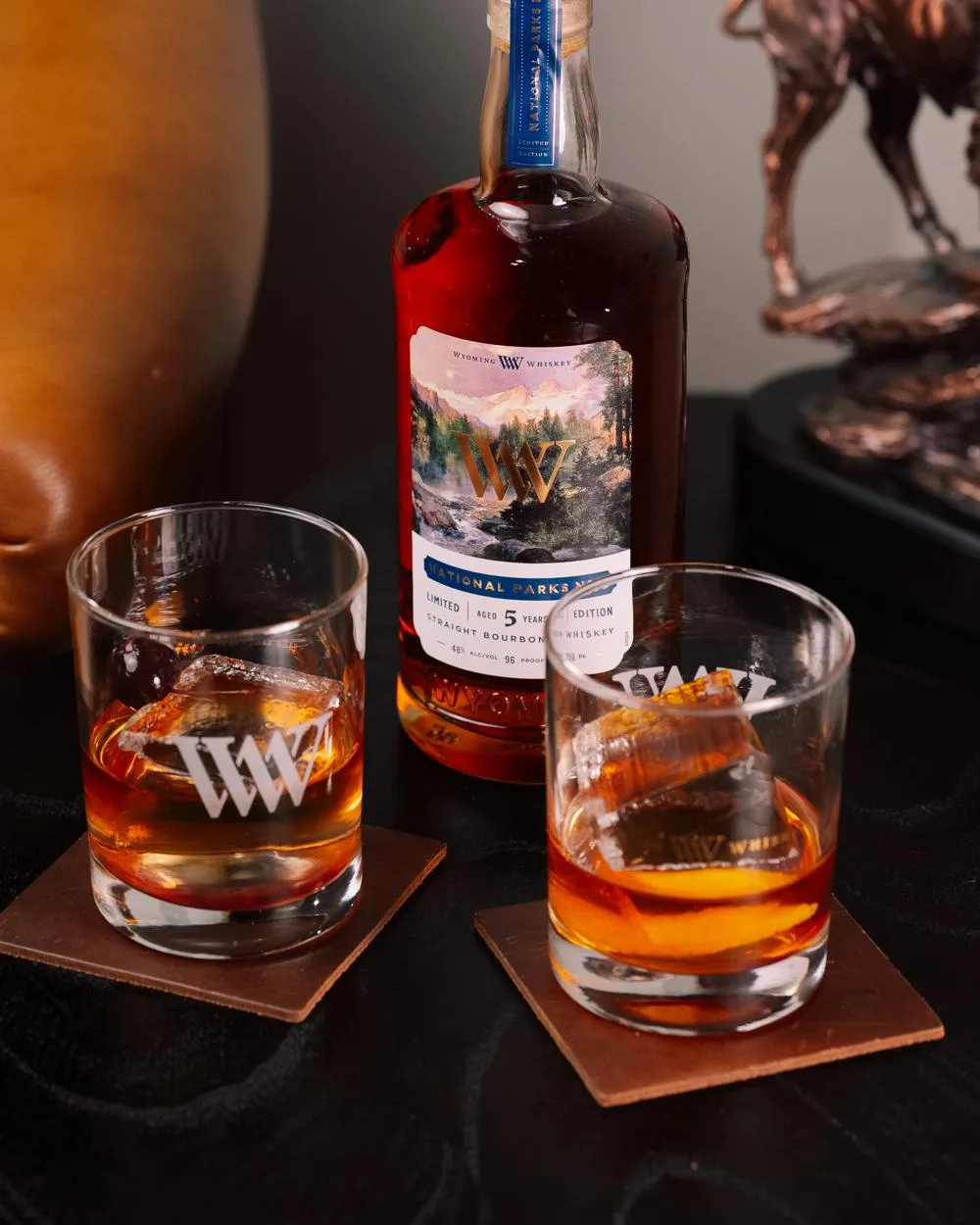 Wyoming Whiskey National Parks No. 5 bottle with Thomas Moran Teton label beside two rocks glasses