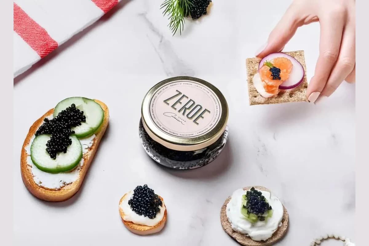 Jar of Zeroe vegan caviar on marble surrounded by caviar-topped canapés